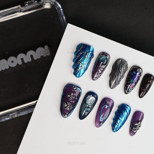 Prometheus press-on nails laid out in blue chrome and purple with armor-like textures and silver cross details