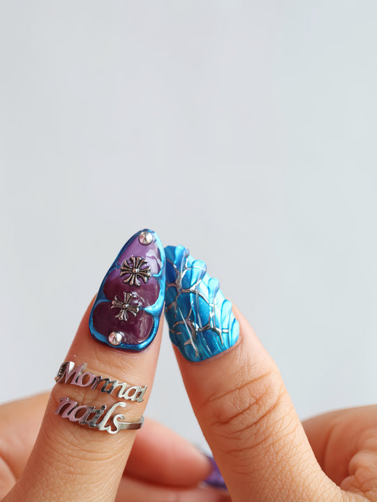 Prometheus press-on nails in close-up on fingers, with metallic blue chrome, purple panels, and silver cross details