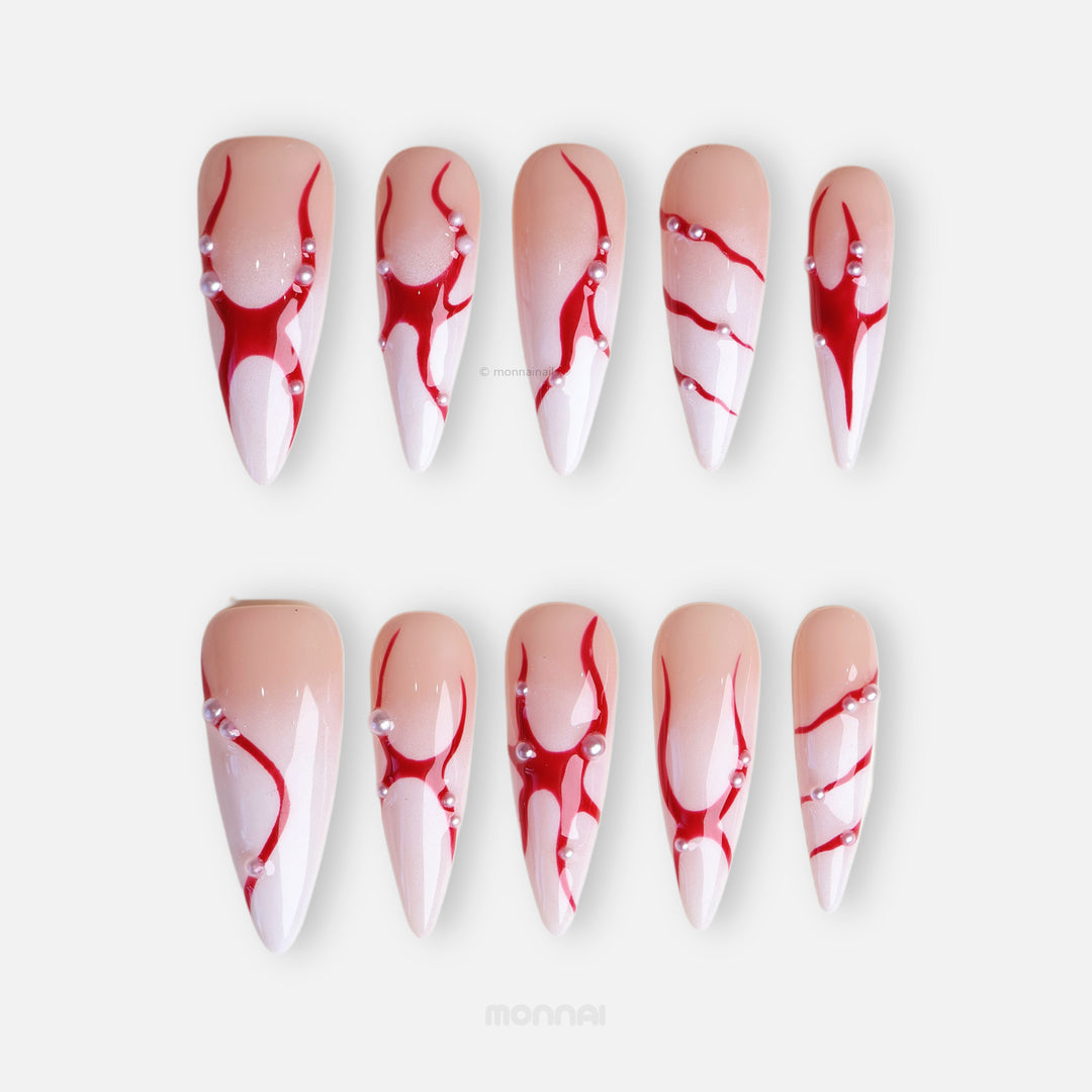 R-ED press-on nails with red fluid lines and scattered pearls, shown laid out in close-up.