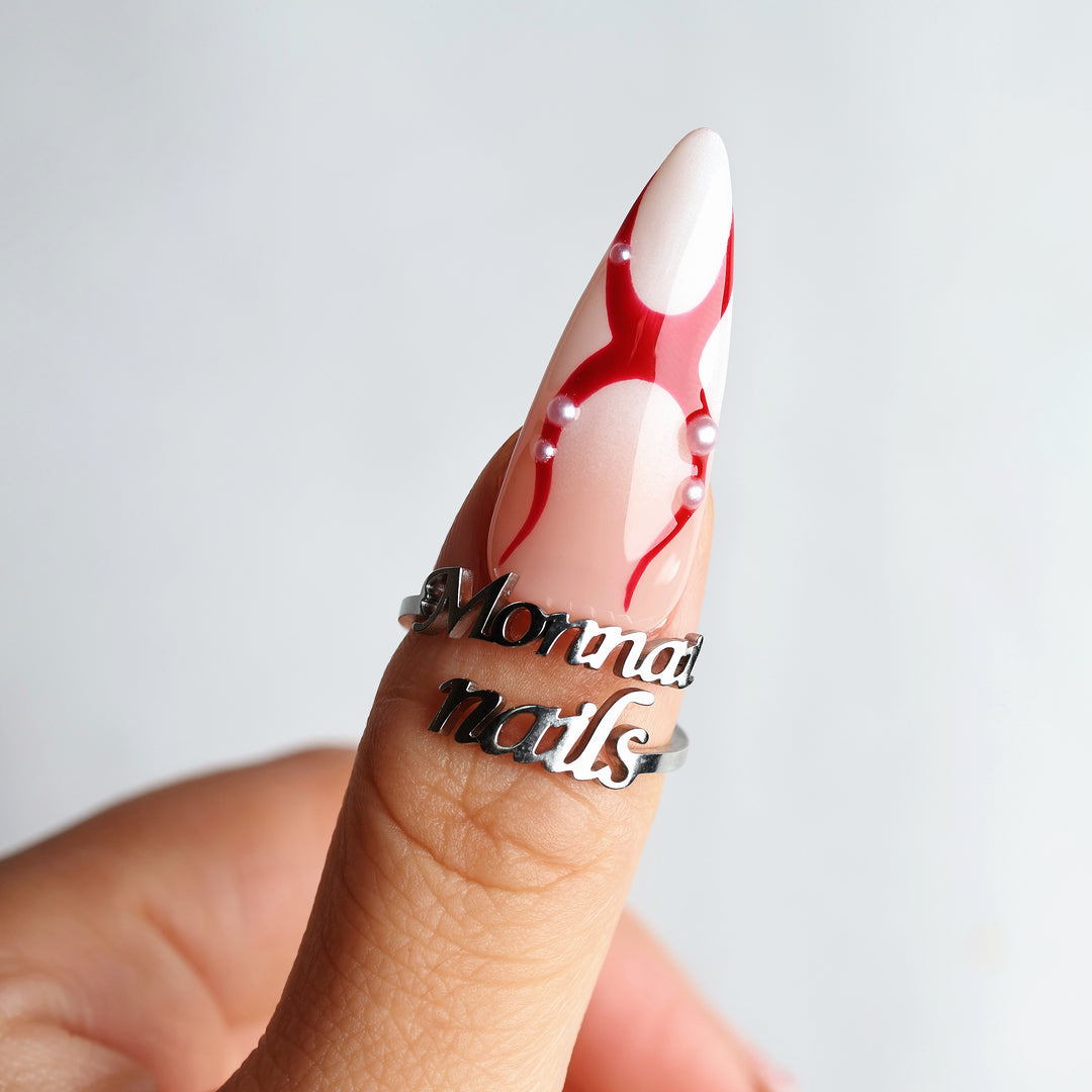 R-ED press-on nails worn on hand, with glossy red lines and scattered pearls in a dark romance style.