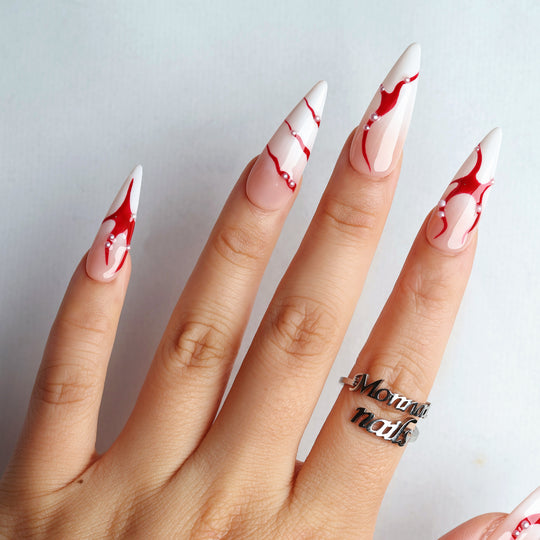 R-ED press-on nails on hand with glossy red fluid lines, pearl accents, and nude-white almond tips in dark romance style