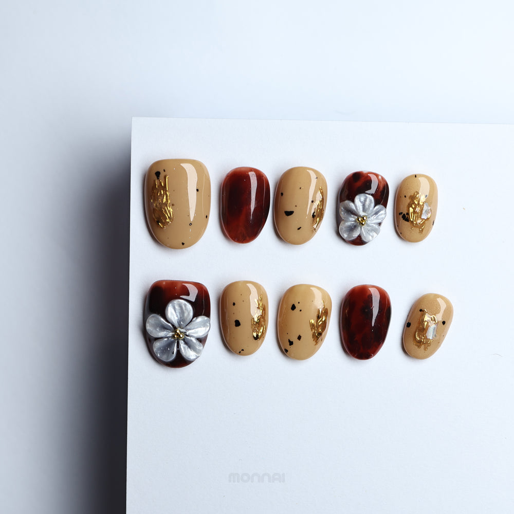 Radiance press-on nails shown laid out, with beige nude, tortoiseshell, gold foil and silver floral accents in a warm vintage style.