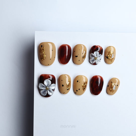 Radiance press-on nails shown laid out, with beige nude, tortoiseshell, gold foil and silver floral accents in a warm vintage style.
