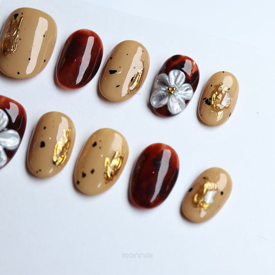 Radiance press-on nails in warm beige and tortoiseshell with gold foil and delicate floral details, laid out