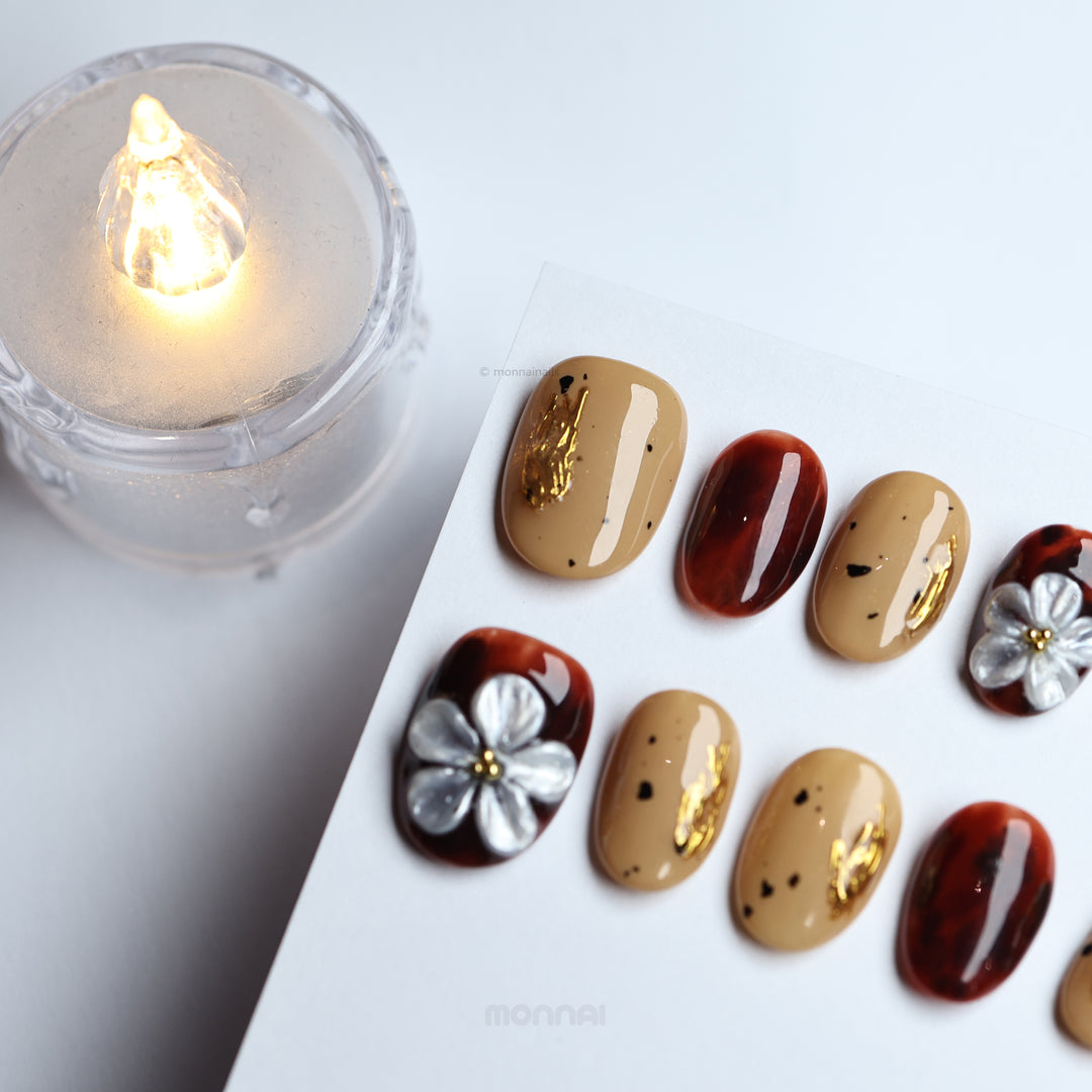 Radiance press-on nails laid out with warm beige and tortoiseshell accents, gold foil, and silver floral details