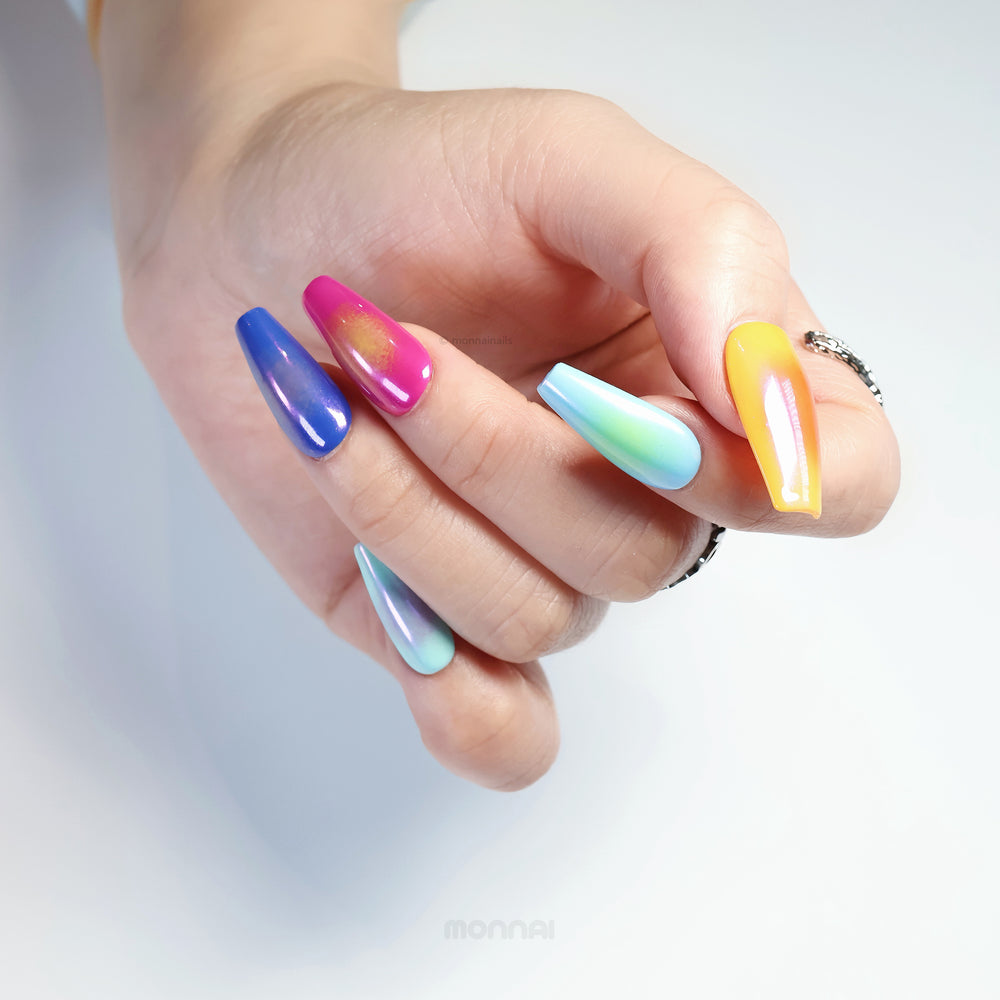 Rainbow Glow press-on nails in hand, showing vivid mismatched rainbow hues with soft aura effects and iridescent chrome finish