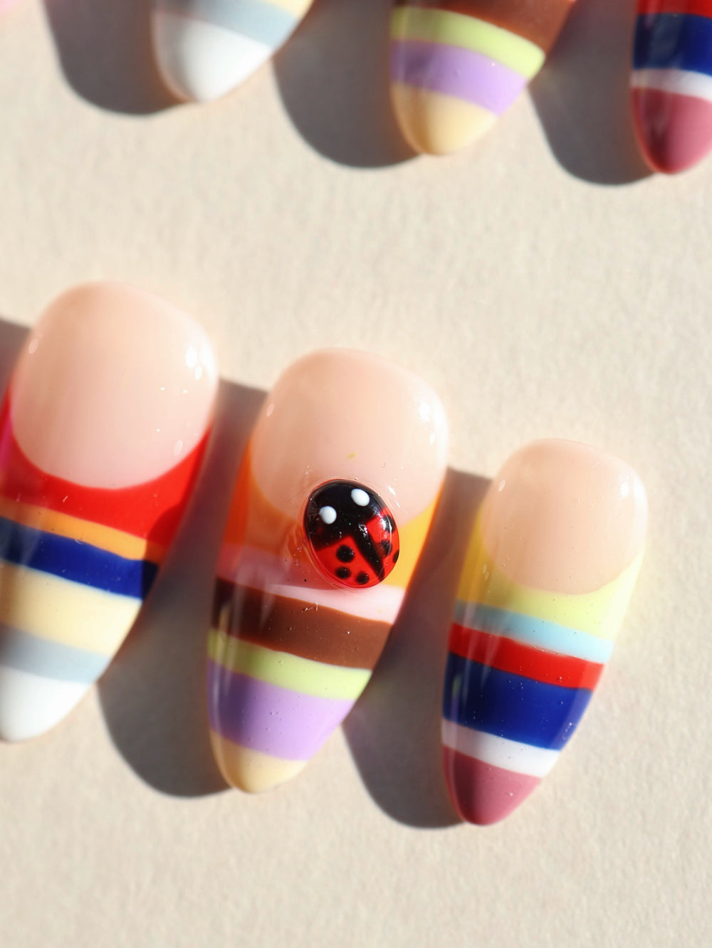 Rainbow Stripes press-on nails, close-up of glossy almond tips with colorful horizontal stripes and a ladybug accent.