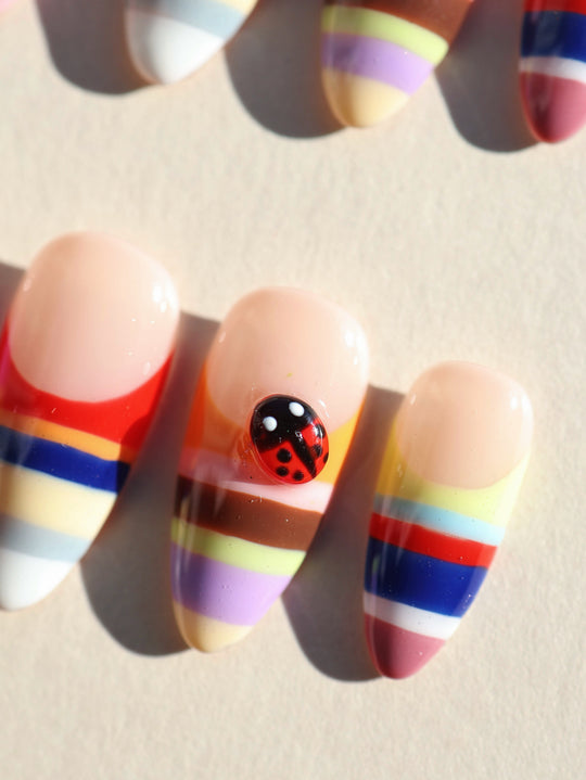 Rainbow Stripes press-on nails, close-up of glossy almond tips with colorful horizontal stripes and a ladybug accent.