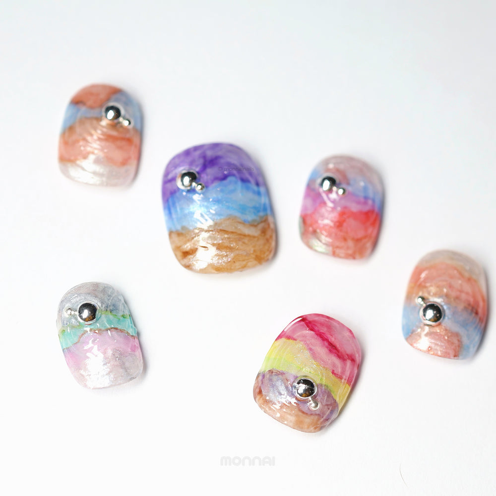 Rainbow Swirl press-on nails laid out, showing abstract iridescent rainbow wavy texture with silver bead accents