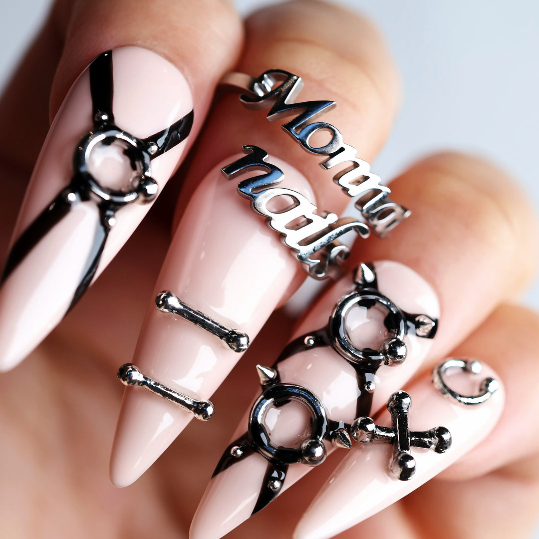 Rebellion press-on nails worn on hand, nude-pink with black harness lines and silver O-ring hardware.
