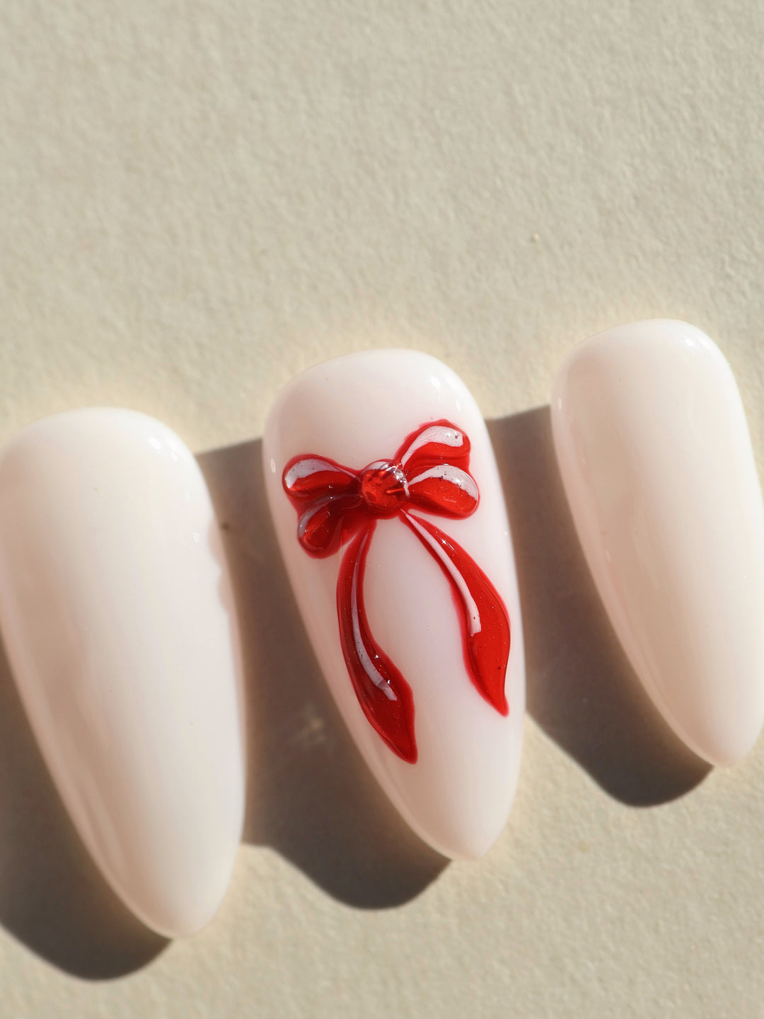 Red Bow press-on nails, close-up of milky white almond nails with a glossy red 3D bow accent