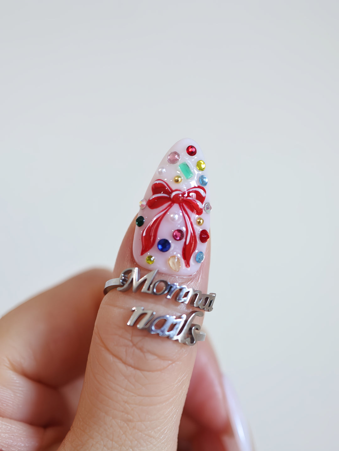 Red Bow press-on nails close-up on hand, milky white almond nail with red bow, colorful rhinestones, glossy finish