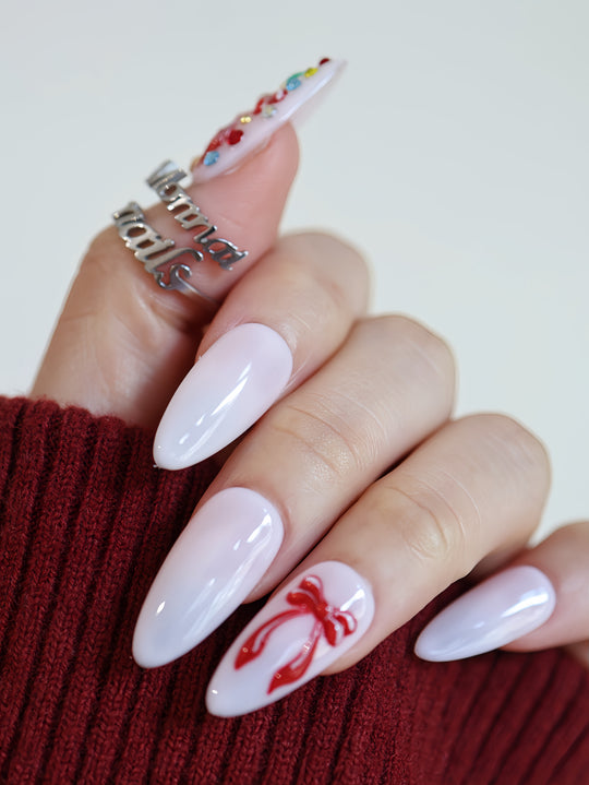 Red Bow press-on nails on hand, milky white almond nails with glossy finish and red ribbon bow accents