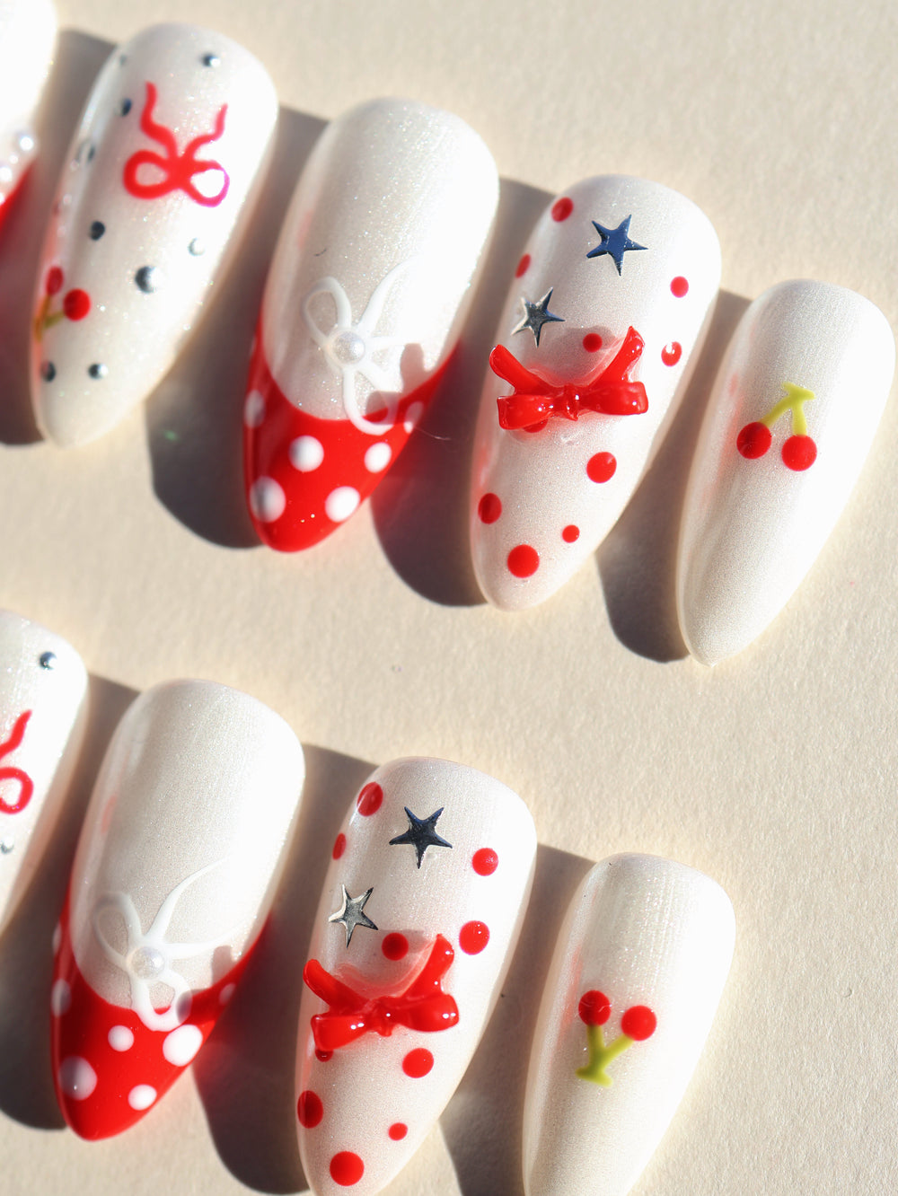 Red Dot Bow press-on nails with pearl white shimmer, red polka dots, cherry motifs, and silver stars