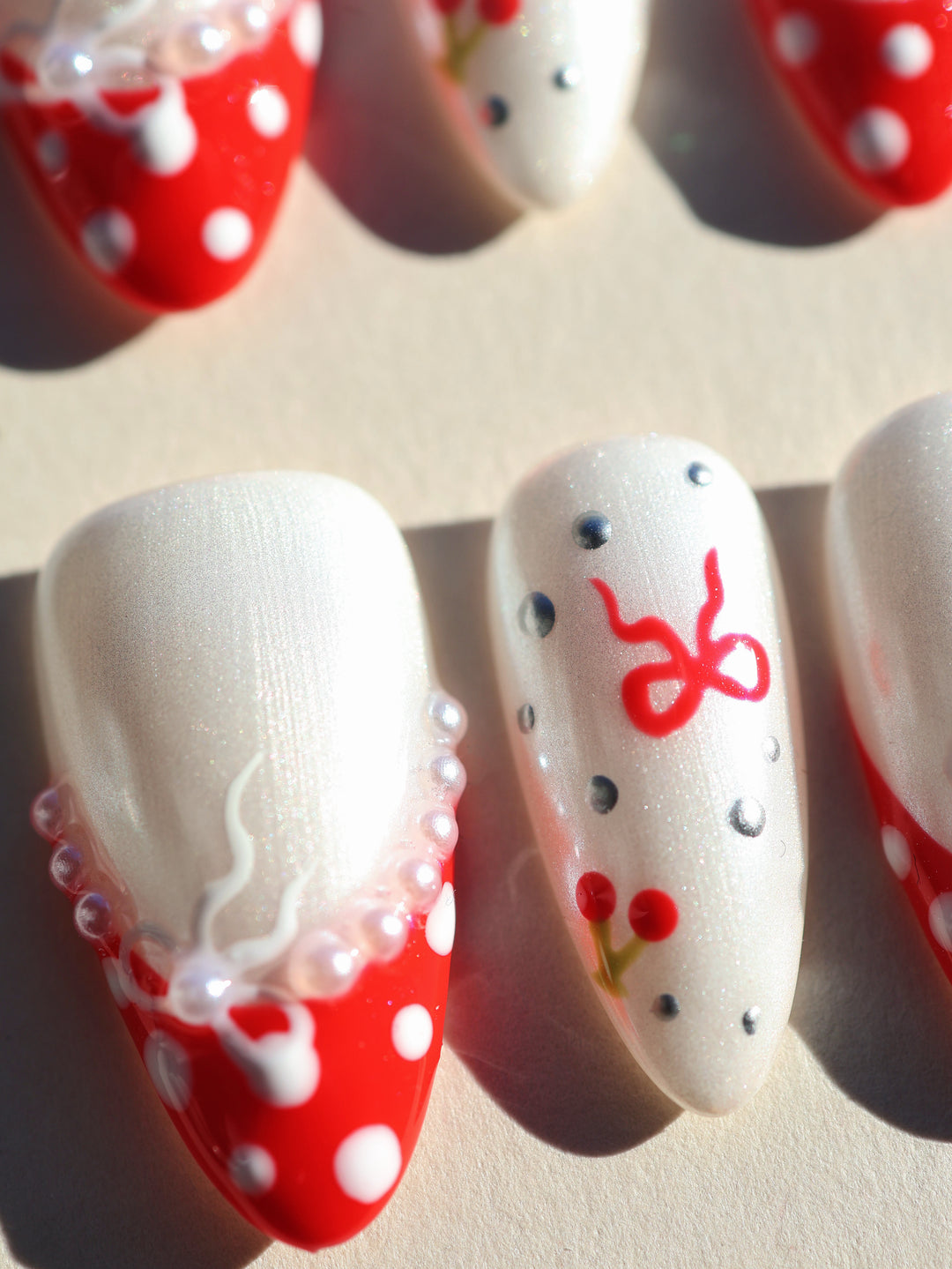 Red Dot Bow press-on nails with pearl white shimmer, red polka dots, and ribbon and cherry details