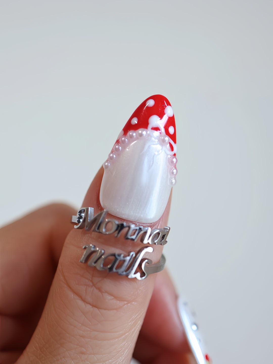 Red Dot Bow press-on nails on hand, pearl white shimmer with red polka dots, silver stars, and pearl accents
