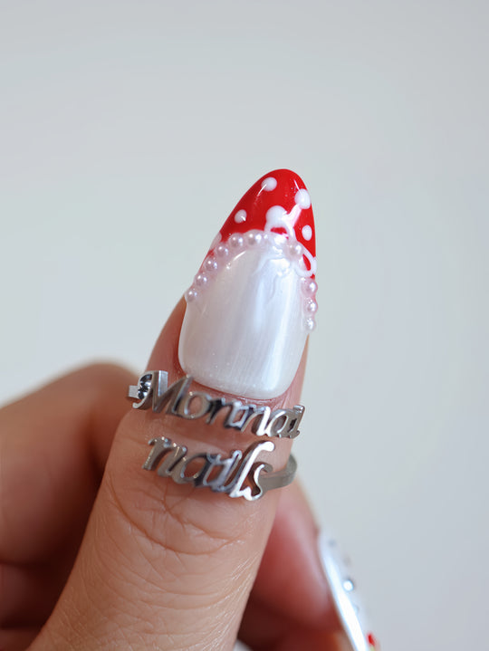 Red Dot Bow press-on nails on hand, pearl white shimmer with red polka dots, silver stars, and pearl accents