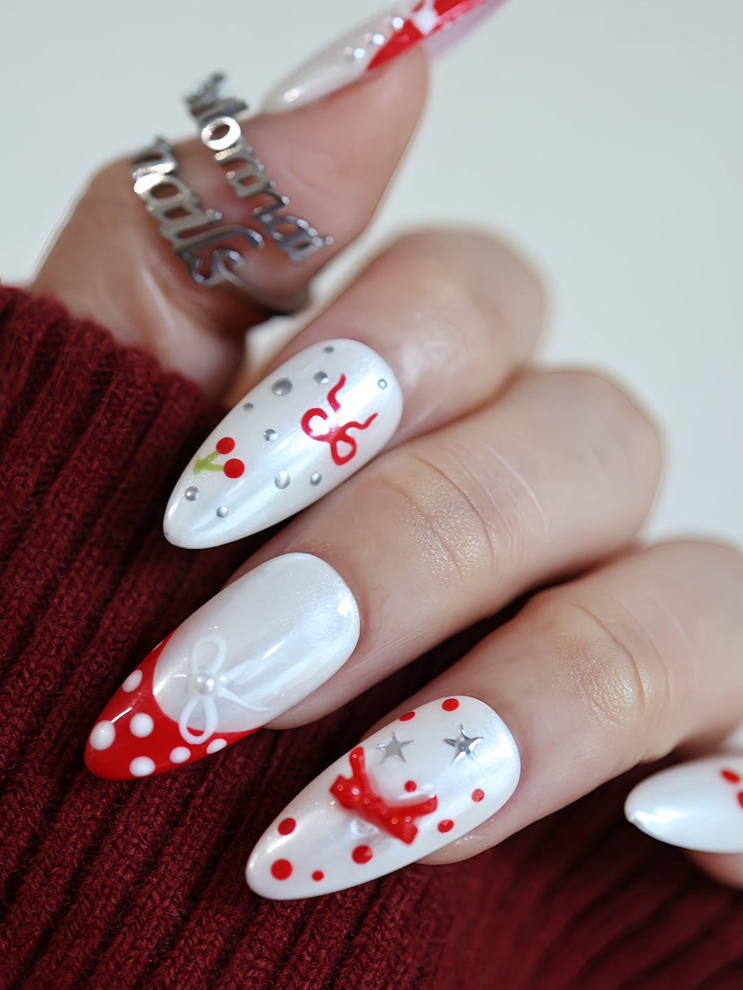 Red Dot Bow press-on nails on hand with white shimmer, red dots, cherries, bows, and silver star accents