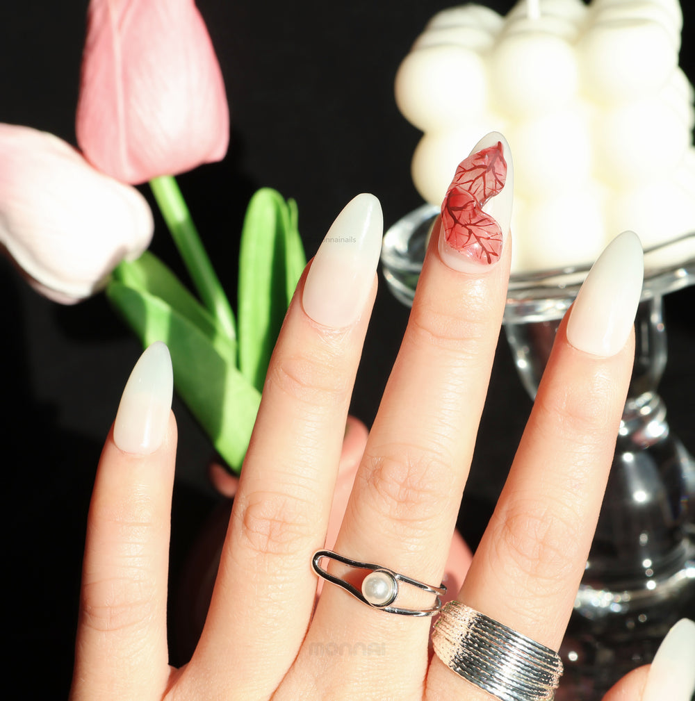 Red Leaves press-on nails worn on hand, milky white base with sheer red leaf detailing and visible veining.