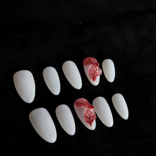 Red Leaves press-on nails in close-up, milky white base with sheer red leaf veining on two nails