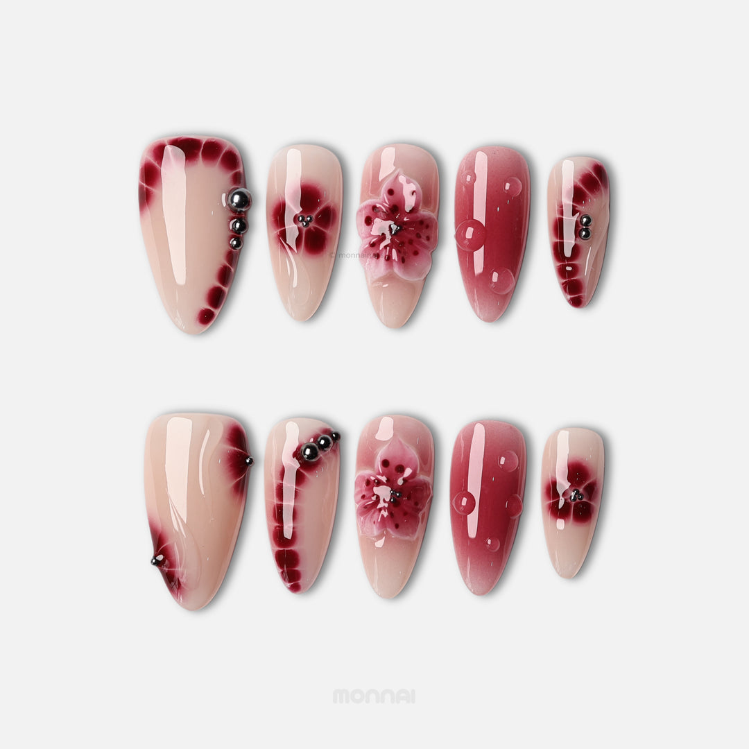 Rosé Mist press-on nails laid out in close-up, with soft red floral gradients, glossy accents, and tiny silver beads on a nude base