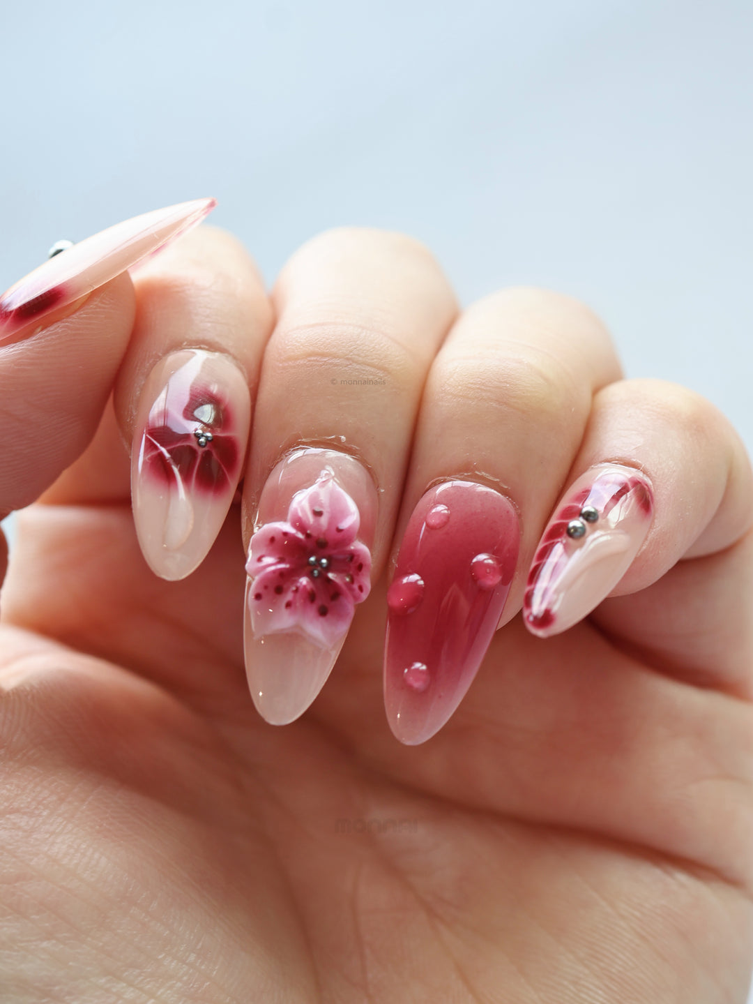 Rosé Mist press-on nails on hand with sheer nude base, soft red floral accents and glossy raised details