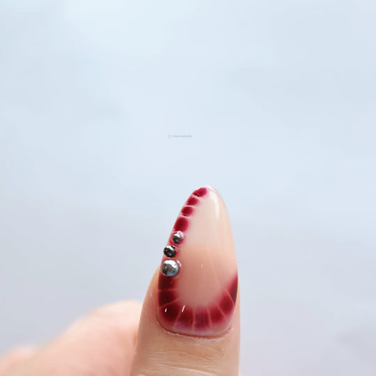 Rosé Mist press-on nails on hand with soft red gradients, glossy accents and silver beads on a sheer nude base.