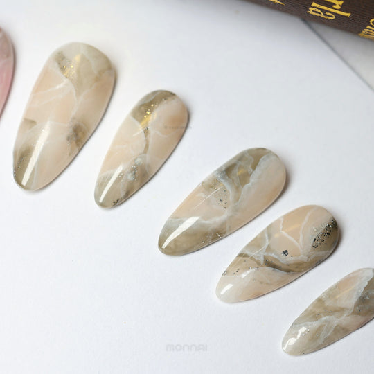 Rose Marble press-on nails laid out in close-up, showing smoky beige-pink marble veining with silver glitter accents.