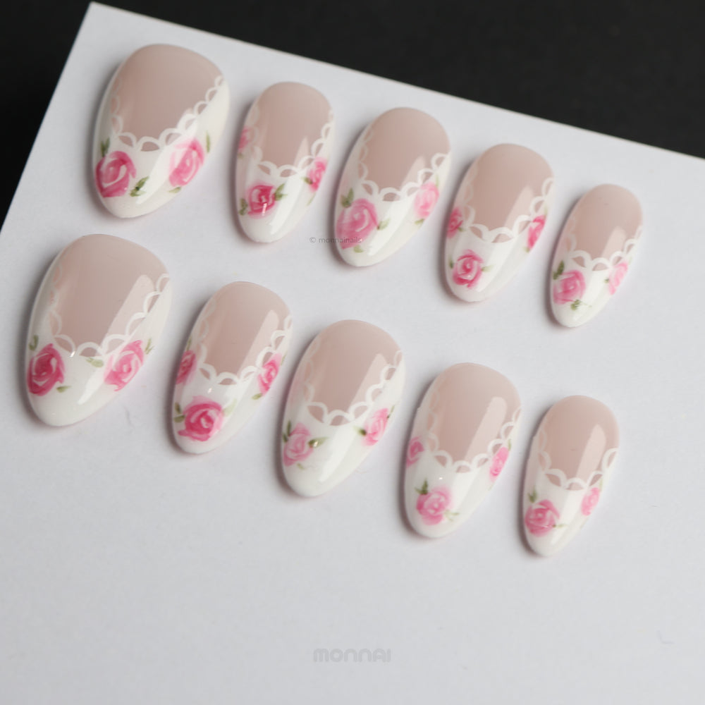 Rosy Lace press-on nails laid out in close-up, with nude and white floral French tips and lace-inspired edging.