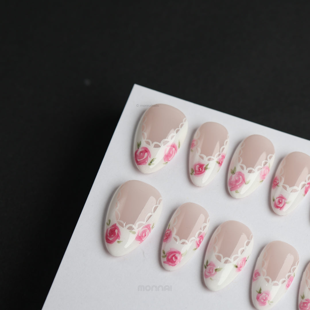 Rosy Lace press-on nails with nude floral accents, white lace-inspired edging, shown laid out in close-up
