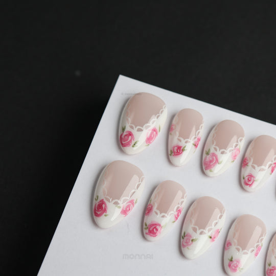 Rosy Lace press-on nails with nude floral accents, white lace-inspired edging, shown laid out in close-up