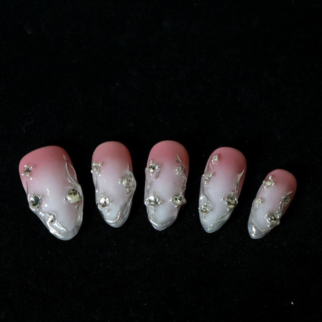 Rosy Metallic Touch press-on nails laid out, showing pink shimmer gradient, fluid 3D edges, and clear rhinestones.