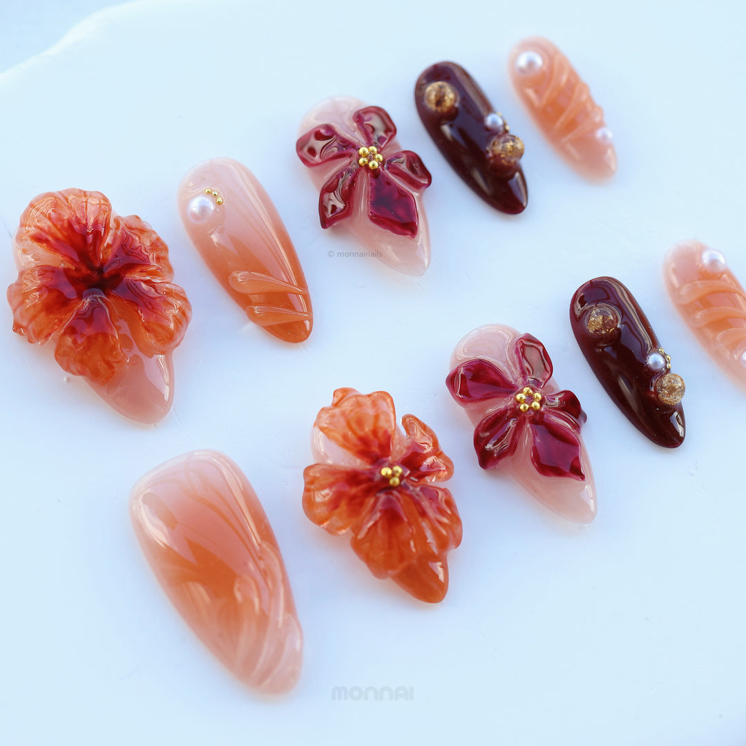 Rustic Elegance press-on nails laid out in coral and deep berry floral designs with glossy 3D flowers and gold accents