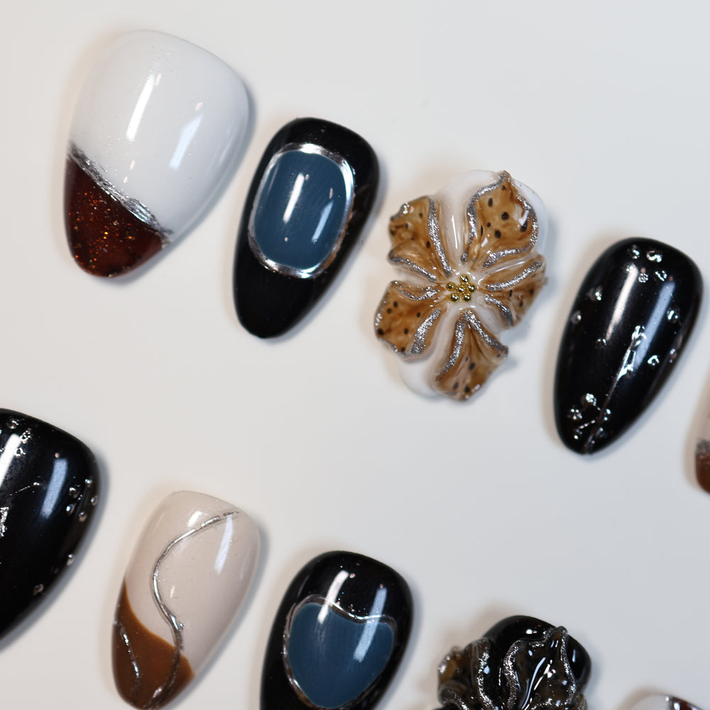 Rustic Luxe press-on nails laid out with black, white, brown and blue sculpted florals, silver edging and linework.