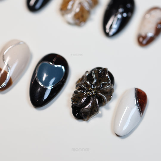 Rustic Luxe press-on nails laid out in close-up, with black, white, tortoiseshell, and muted blue sculpted florals.