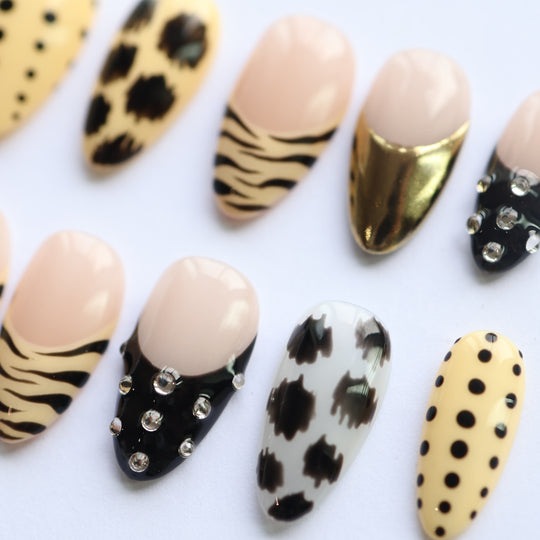 Safari Chic press-on nails laid out in a safari-themed set with zebra stripes, gold chrome, rhinestones, and black polka dots.