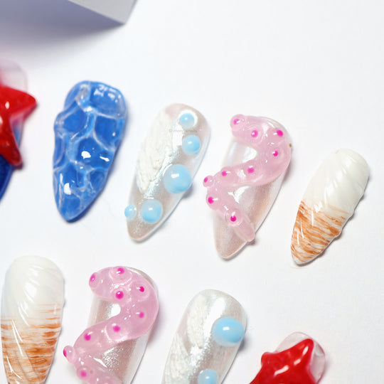 Seaside Fantasy press-on nails laid out in close-up, featuring blue ripples, pink tentacles, red starfish and shell-like white tips.