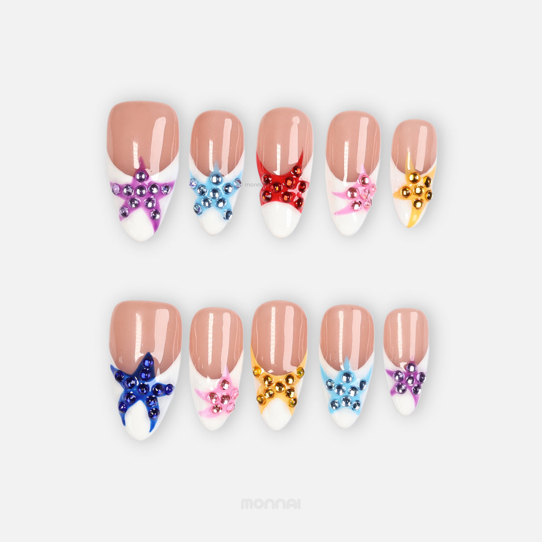 Seaside Starlight press-on nails laid out in a set, with glossy French tips and colorful rhinestone star details.