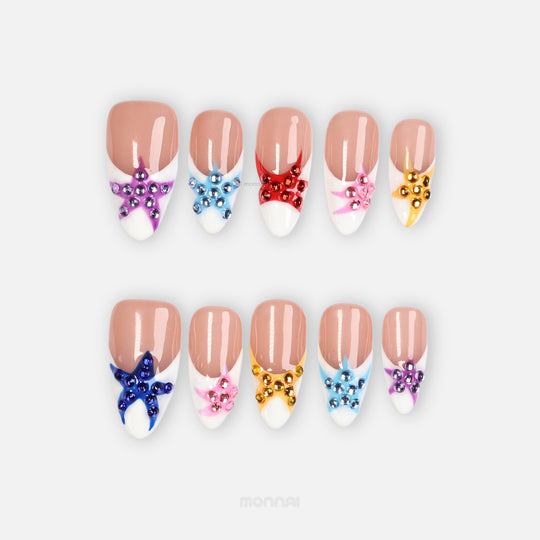 Seaside Starlight press-on nails laid out in a set, with glossy French tips and colorful rhinestone star details.