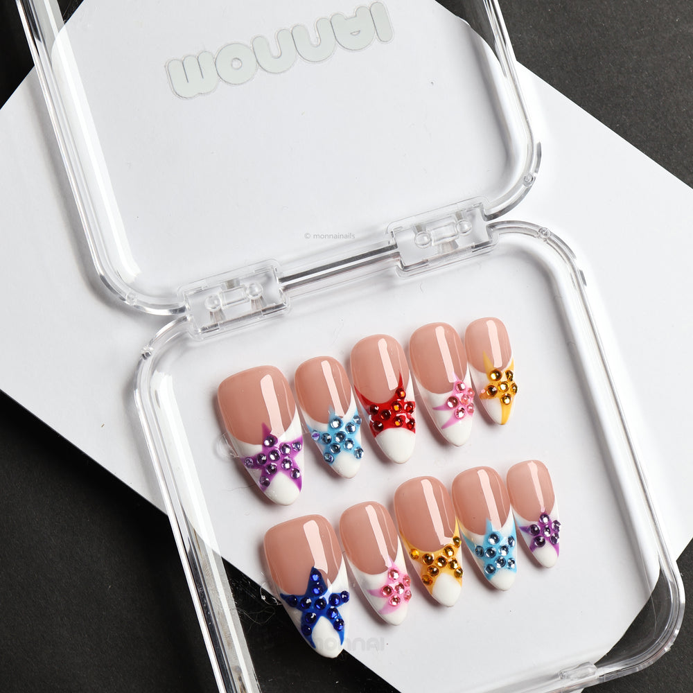 Seaside Starlight press-on nails laid out in a case, featuring glossy white French tips with colorful rhinestone star details.