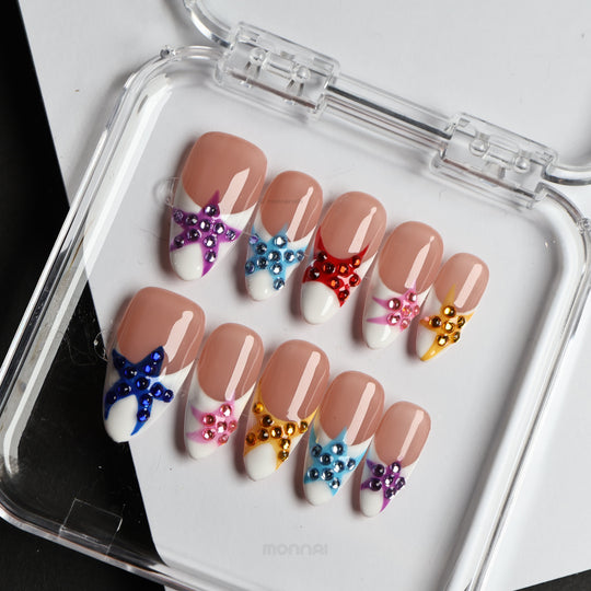 Seaside Starlight press-on nails laid out with glossy white French tips and colorful rhinestone star details