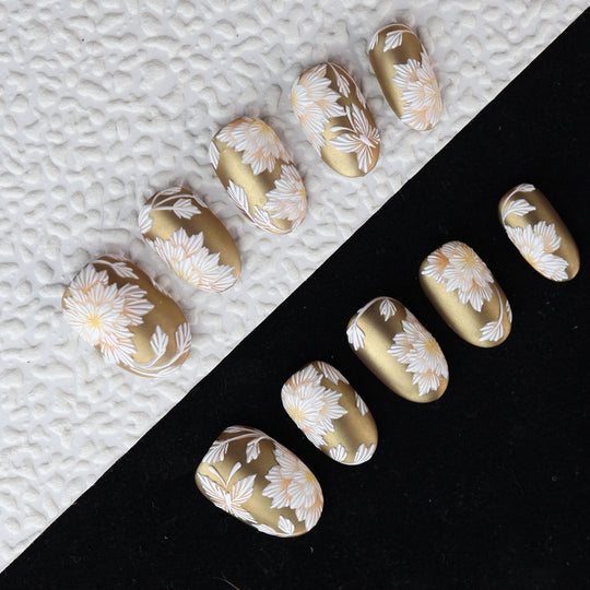 Silk &amp; Stitches press-on nails with gold chrome and white floral embroidery-style details, shown laid out