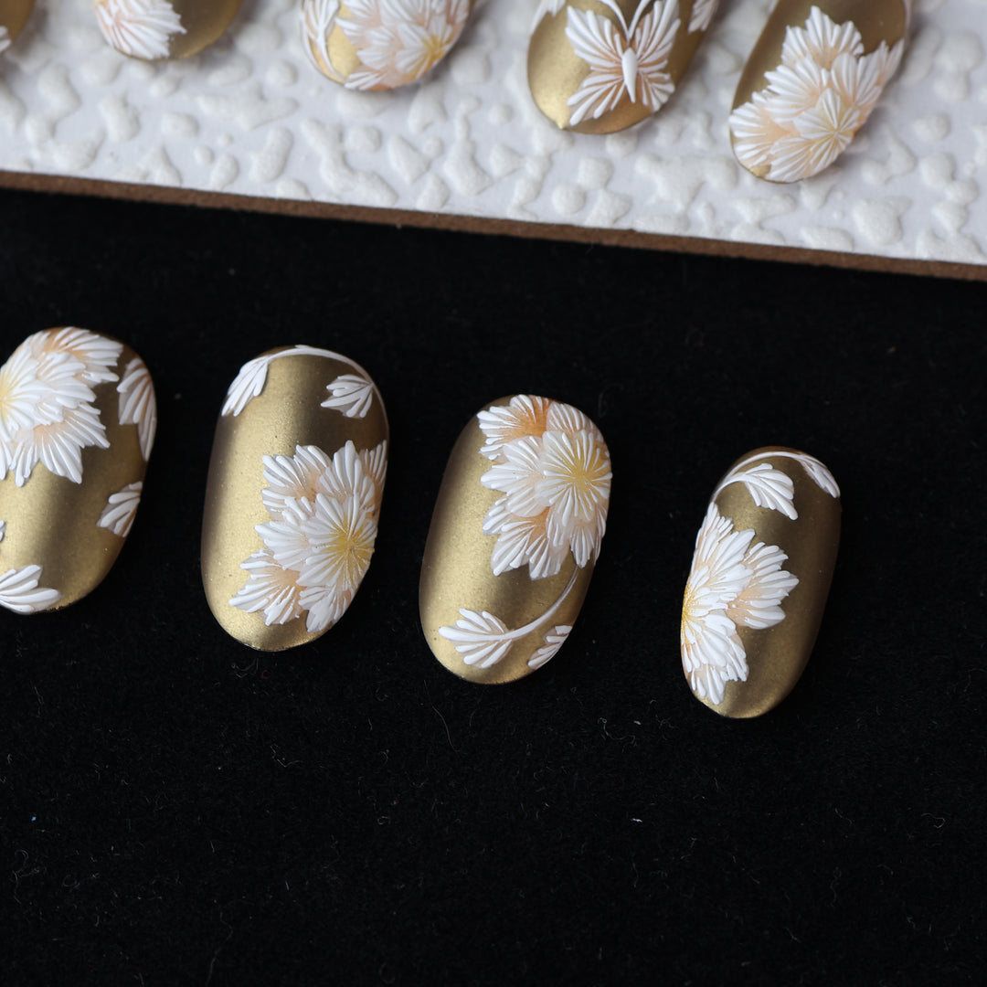 Silk &amp; Stitches press-on nails in gold chrome with white floral embroidery laid out in close-up