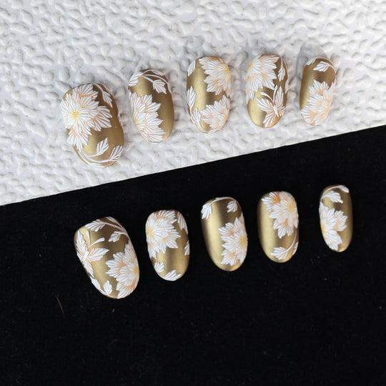 Silk &amp; Stitches press-on nails with gold chrome and white floral embroidery laid out in close-up