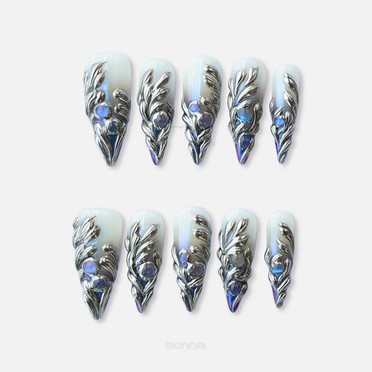 Silver Dreams press-on nails laid out, with chrome feather textures and icy iridescent blue accents.