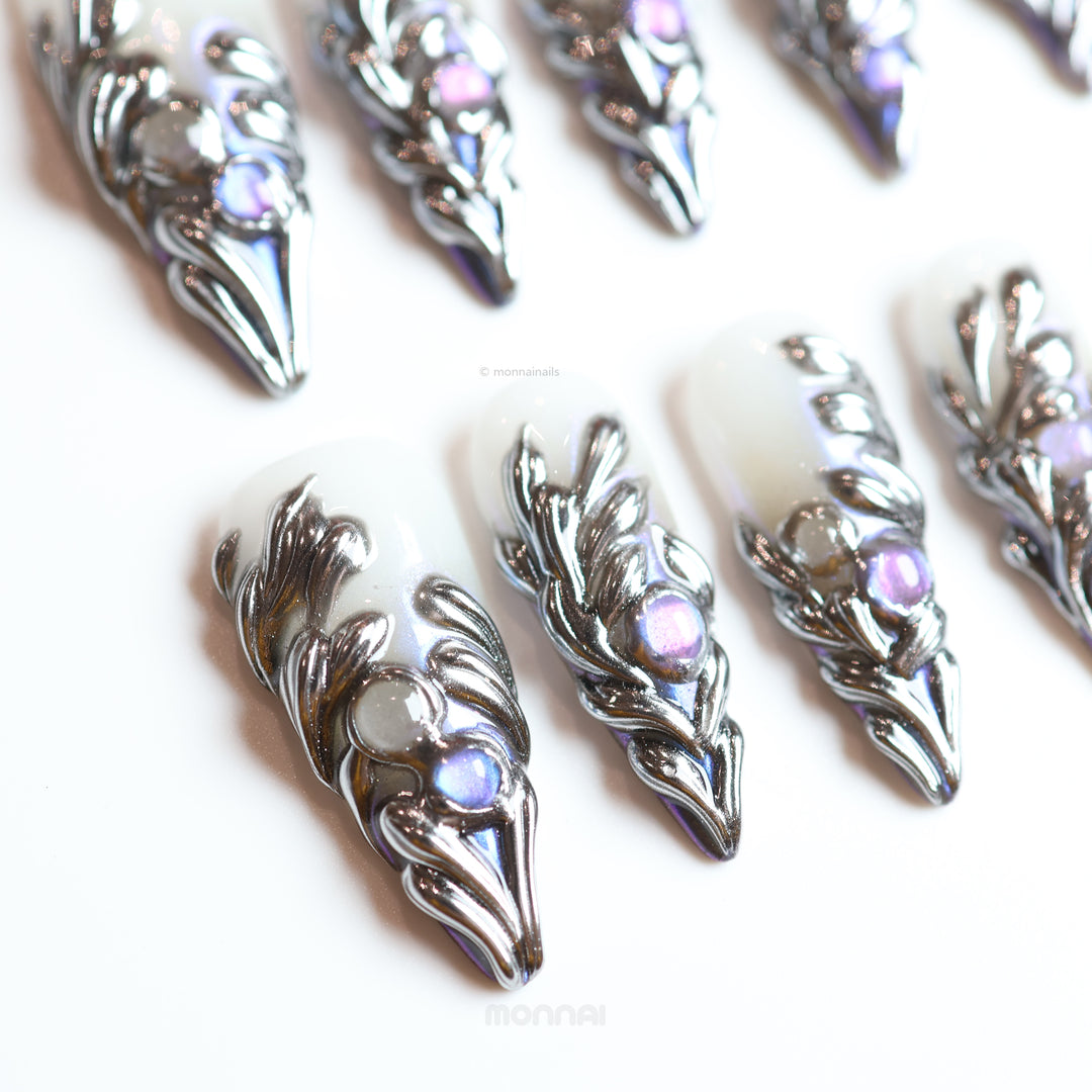Silver Dreams press-on nails with silver chrome feathers and iridescent accents laid out in close-up