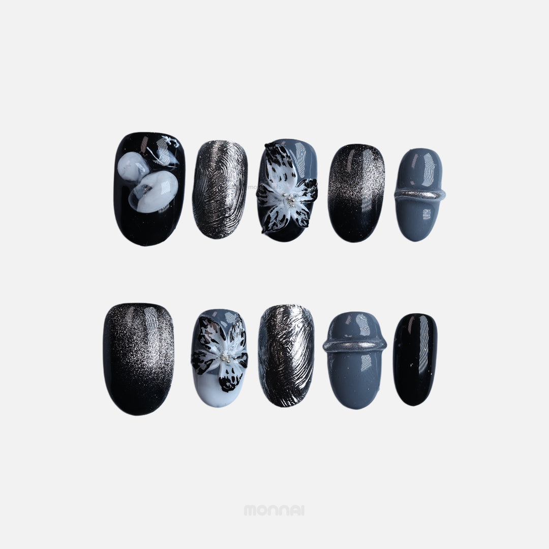 Silver Eclipse press-on nails laid out in moody black, grey, and silver with floral details and chrome accents