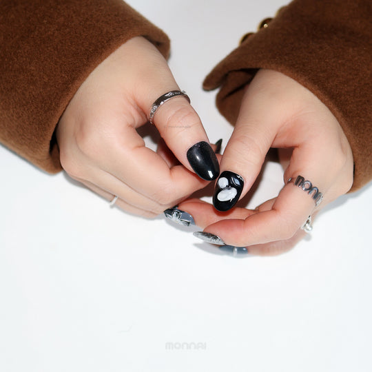 Silver Eclipse press-on nails on hands, glossy black with white floral accents and chrome details in a moody sleek style.