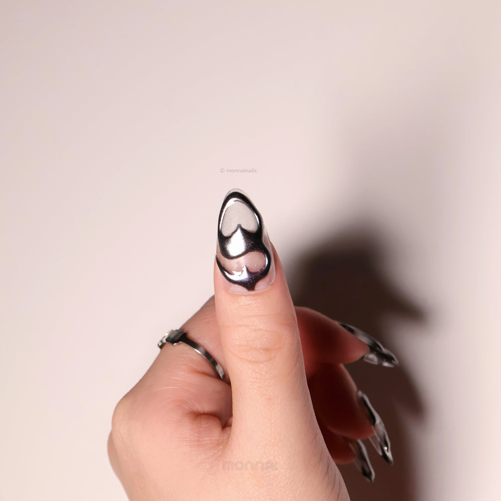 Silver Mystic Flow press-on nails in close-up, featuring liquid chrome silver sculptural hearts and glossy futuristic curves.