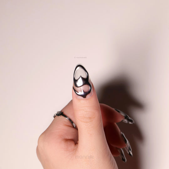 Silver Mystic Flow press-on nails in close-up, featuring liquid chrome silver sculptural hearts and glossy futuristic curves.